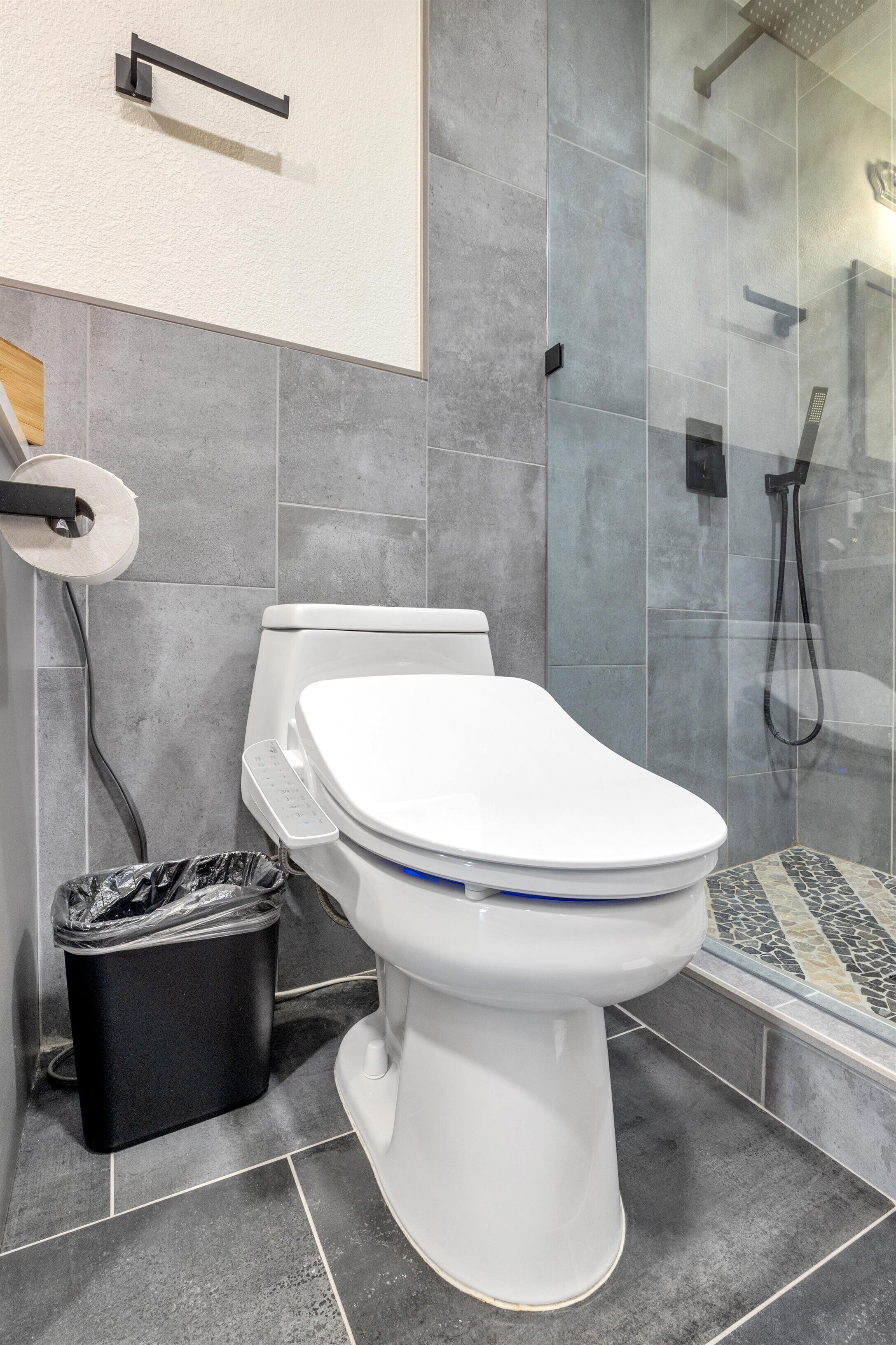 A modern bathroom with a toilet, a trash bin, and a glass-enclosed shower area.