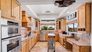 A modern kitchen with wooden cabinets, stainless steel appliances, and a large window providing a view of the outdoors. - Luxury one level villa on 1/2 acre 12 min from The Strip (Las Vegas)