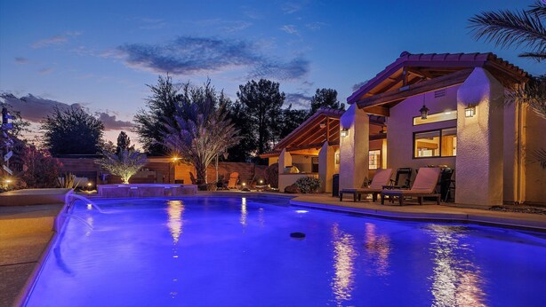 A swimming pool with a blue-lit water feature, a covered patio with lounge chairs, and a building with a stucco exterior and wooden beams. - Luxury one level villa on 1/2 acre 12 min from The Strip (Las Vegas)