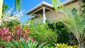 A house with a covered porch, surrounded by lush tropical plants and a clear blue sky. - Lawson Rock - Yellowfish 211 2 Bedroom Condo by RedAwning (Roatan)