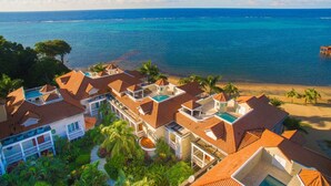 A coastal resort with multiple buildings featuring red-tiled roofs, a swimming pool, and a beach view. - Lawson Rock - Yellowfish 211 2 Bedroom Condo by RedAwning (Roatan)