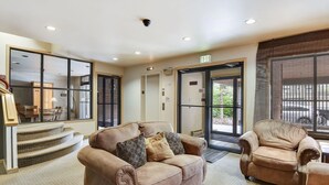 Uma sala de estar espaçosa com sofá e poltrona bege, escada que leva a um andar superior e janelas amplas com vista para o exterior.