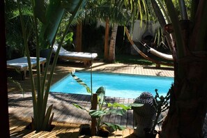 A pool with lounge chairs, surrounded by tropical plants and a wooden deck. - Yuca-Spa  Studio de charme & spa-jacuzzi (Saint Paul)