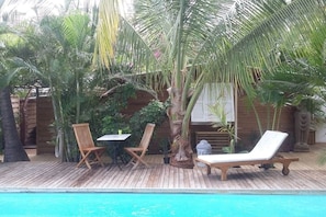A wooden deck with a pool, two wooden chairs, a table, and a lounge chair.