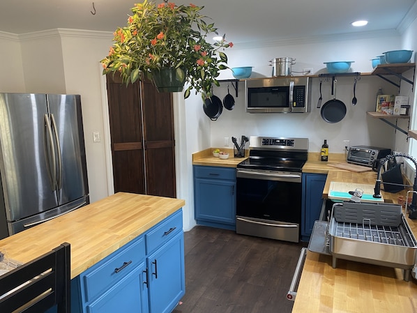 Una cocina moderna con un refrigerador de acero inoxidable, un microondas, una estufa y un horno tostador. Hay una encimera de madera, armarios azules y una planta colgante.