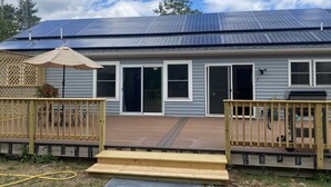 Uma casa com telhado solar, um deck com grade de madeira e uma porta de correr de vidro.