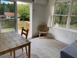 Una habitación con una mesa de madera, una silla, un ventanal y vistas a una terraza de madera y árboles.