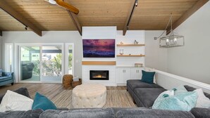 A spacious living room with a fireplace, a ceiling fan, and a large window overlooking a balcony.