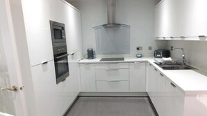A modern kitchen with white cabinets, a built-in oven, a coffee maker, and a sink.