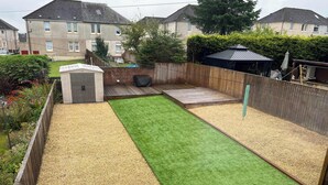 A fenced backyard with artificial grass, a gravel area, and a small shed.