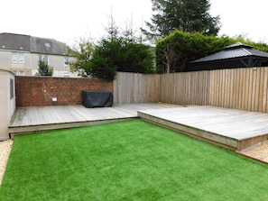 A backyard with a wooden deck, a brick wall, and a green lawn. - Beautiful 3 bedroom home with large garden. 35 mins to Glasgow & Edinburgh. (Shotts)