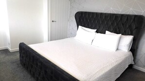 A bed with a black headboard and white bedding, a door, and a geometric-patterned wall.