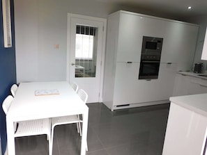 A compact kitchen with white cabinets, a built-in oven, and a dining area with a white table and chairs. - Beautiful 3 bedroom home with large garden. 35 mins to Glasgow & Edinburgh. (Shotts)