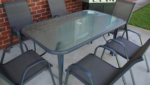 An outdoor patio with a glass-top table and four metal chairs. - Wagga Showground Villas (Turvey Park)