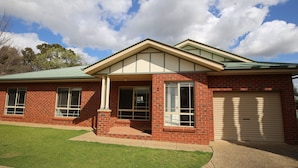 A two-story brick house with a green roof, a garage, and a well-maintained lawn. - Wagga Showground Villas (Turvey Park)
