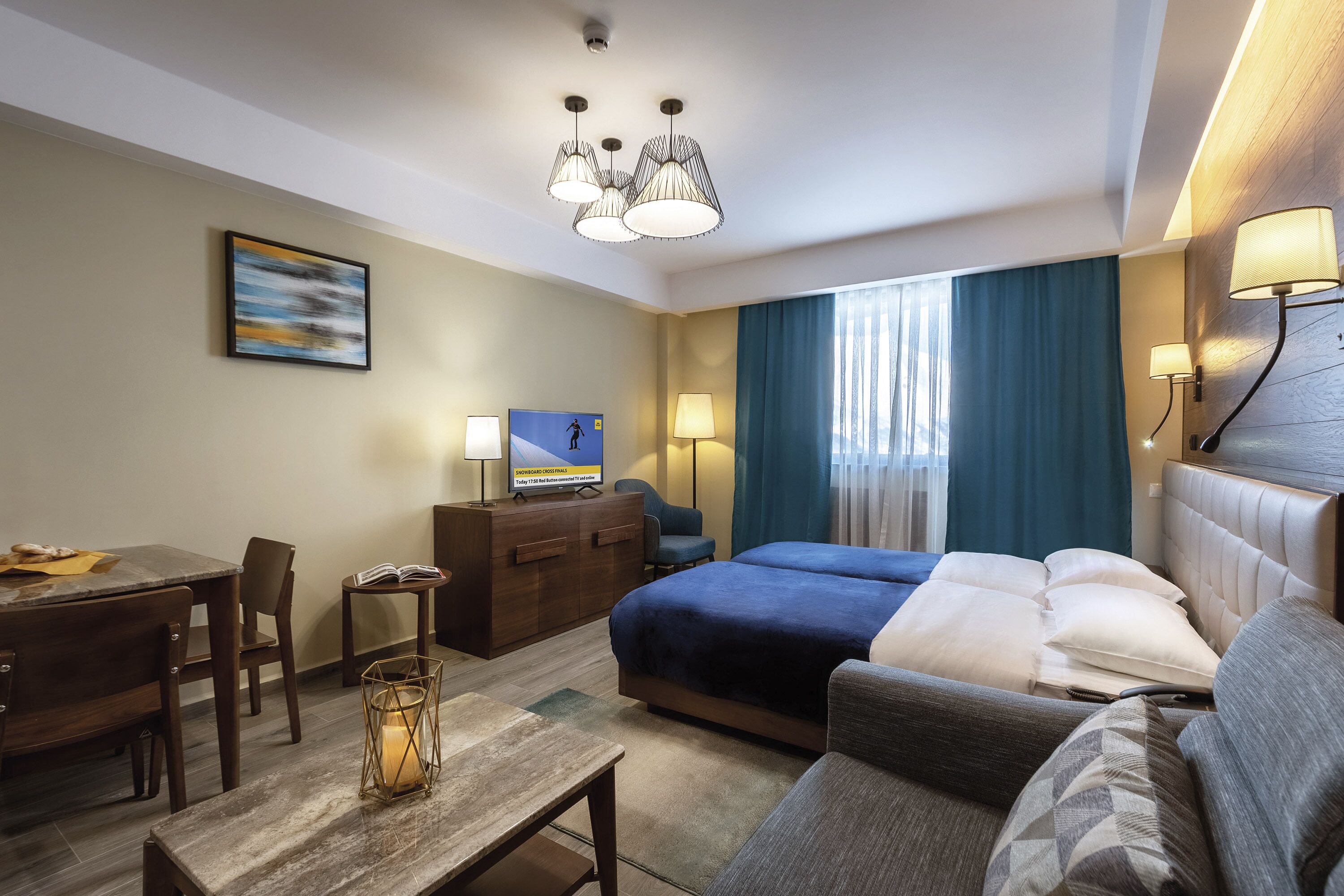 A hotel room with a bed, a desk, a chair, a lamp, and a television.
