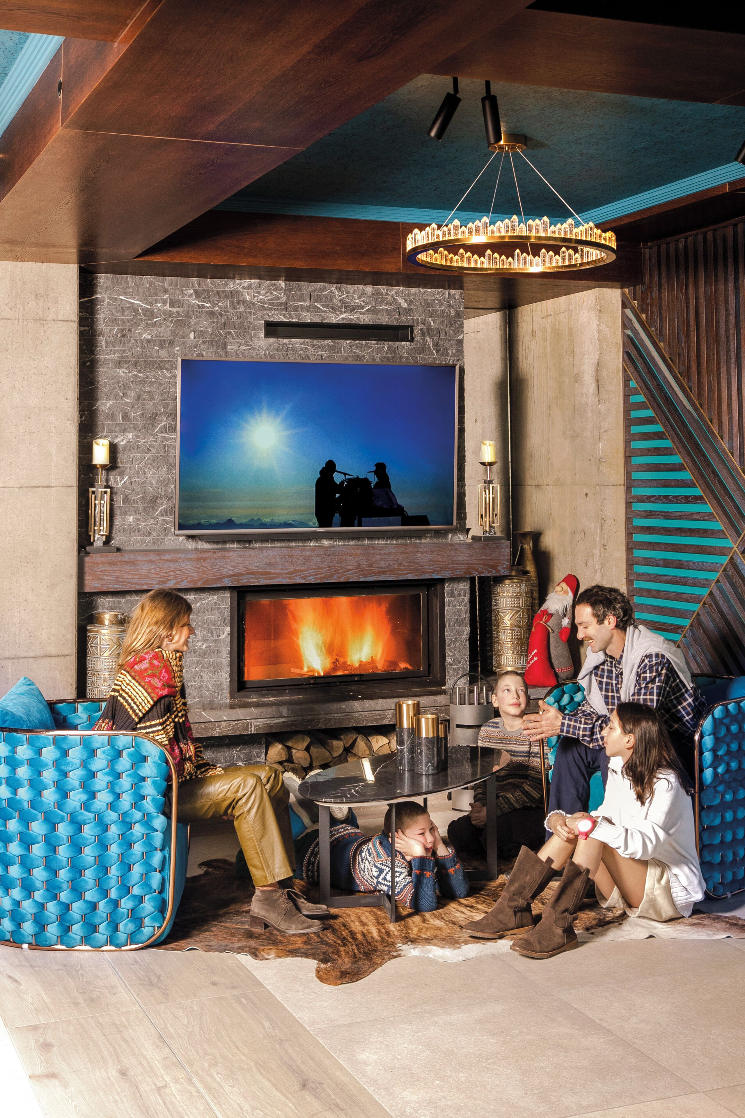 A family gathered around a fireplace with a TV above it, in a room with a stone wall and a wooden ceiling.