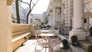 Une terrasse extérieure avec une table et des chaises, un petit escalier et une vue sur les bâtiments en arrière-plan.