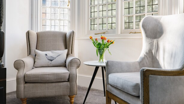 Une pièce comprenant deux fauteuils, une petite table ornée d’un vase de fleurs et une fenêtre donnant sur un beau paysage.