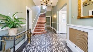 Un grand escalier orné d’un motif au sol menant à une porte, un lustre et une plante en pot.