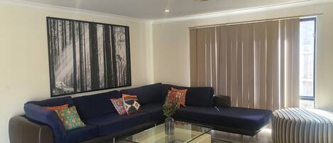 A modern living room with a dark blue sofa, colorful cushions, a glass coffee table, and a large abstract painting on the wall.