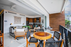 A modern living space with a balcony, a dining area with a round wooden table, and a kitchen with dark wood cabinets.