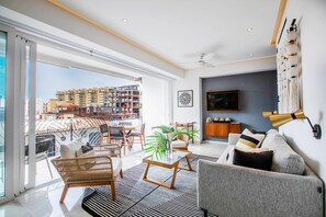 Ein modernes Wohnzimmer mit einer Couch, einem Couchtisch, Sesseln, einem Flachbildfernseher und einem großen Fenster mit Blick auf die Stadt.