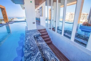 A modern poolside area with a marble-tiled bench, wooden steps, and a view of the sea.