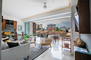 A modern living room with a dining area, a kitchen, and a balcony with outdoor seating. - NEW 1 BR w/pool and gym @ Desire (Puerto Vallarta)