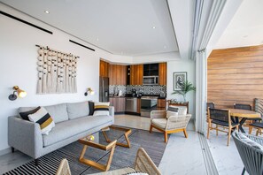 Een moderne woonkamer met een bank, salontafel en stoelen, een keuken met houten keukenkastjes en een magnetron, en een eethoek met een tafel en stoelen.