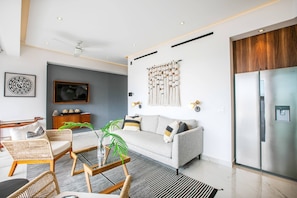 A modern living room with a grey sofa, wicker chairs, a glass coffee table, and a large flat-screen TV.