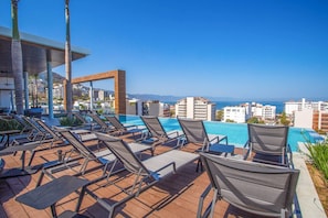 A poolside area with lounge chairs and a view of the ocean and buildings.
