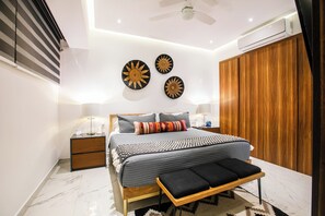 A modern bedroom with a bed, bedside tables, a bench, a ceiling fan, and wall decorations. - NEW 1 BR w/pool and gym @ Desire (Puerto Vallarta)