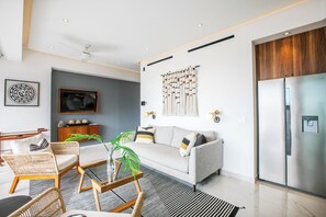 A modern living room with a grey sofa, wicker chairs, a glass coffee table, and a large flat-screen TV mounted on the wall. - NEW 1 BR w/pool and gym @ Desire (Puerto Vallarta)