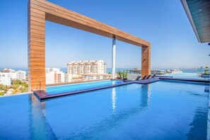 A rooftop infinity pool with a wooden pergola structure, overlooking a cityscape and the sea. - NEW 1 BR w/pool and gym @ Desire (Puerto Vallarta)