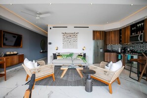 A modern living room with a sofa set, a coffee table, and a dining area with a kitchen in the background. - NEW 1 BR w/pool and gym @ Desire (Puerto Vallarta)