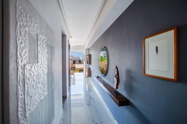 A hallway with a marble floor, a textured wall, and a view of buildings outside.