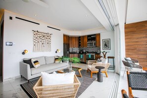 A modern living room with a sofa, chairs, a coffee table, and a kitchen in the background. - NEW 1 BR w/pool and gym @ Desire (Puerto Vallarta)