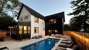 A two-story house with a swimming pool, outdoor seating, and a wooden deck. - New luxury home steps to downtown w/yr round heated pool (New Buffalo)