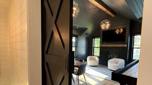 A modern interior with a black door, wooden flooring, a dining area with chairs, a sofa, and pendant lighting. - New luxury home steps to downtown w/yr round heated pool (New Buffalo)