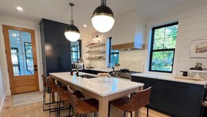 A modern kitchen with a central island, dark cabinetry, and pendant lighting. - New luxury home steps to downtown w/yr round heated pool (New Buffalo)