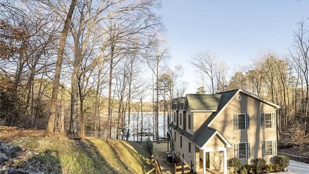 A two-story house with a small attached garage and a porch, surrounded by trees and a lake. - NEW!Lakefront retreat with huge dock, private cove. Perfect for Clemson Football (Central)