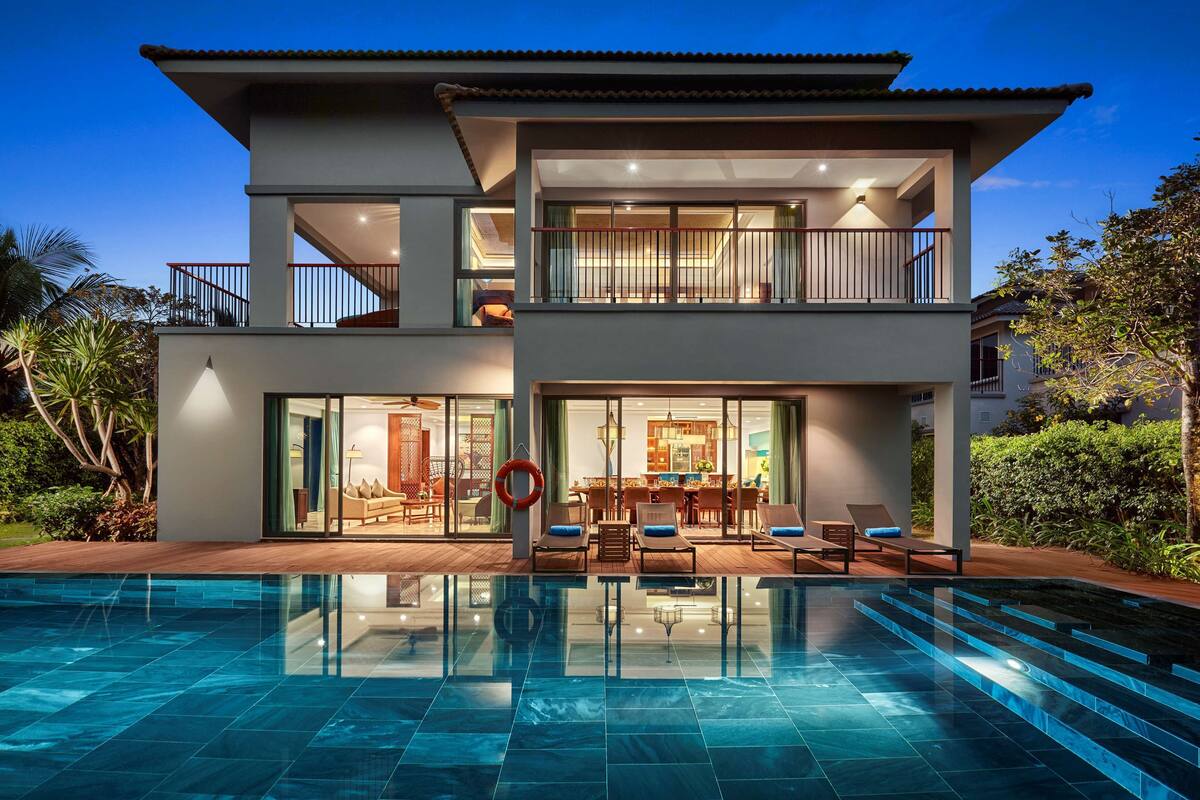 A modern two-story house with a swimming pool, large glass windows, and a balcony.