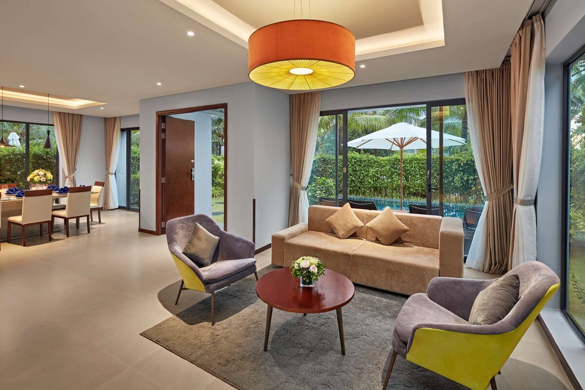 A modern living room with a sofa, two armchairs, a coffee table, and a large window with a view of greenery.
