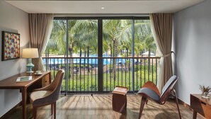 A modern hotel room with a balcony, a desk, two chairs, and a view of a pool and palm trees. - Best Western Premier Sonasea Villas Phu Quoc (Phu Quoc)