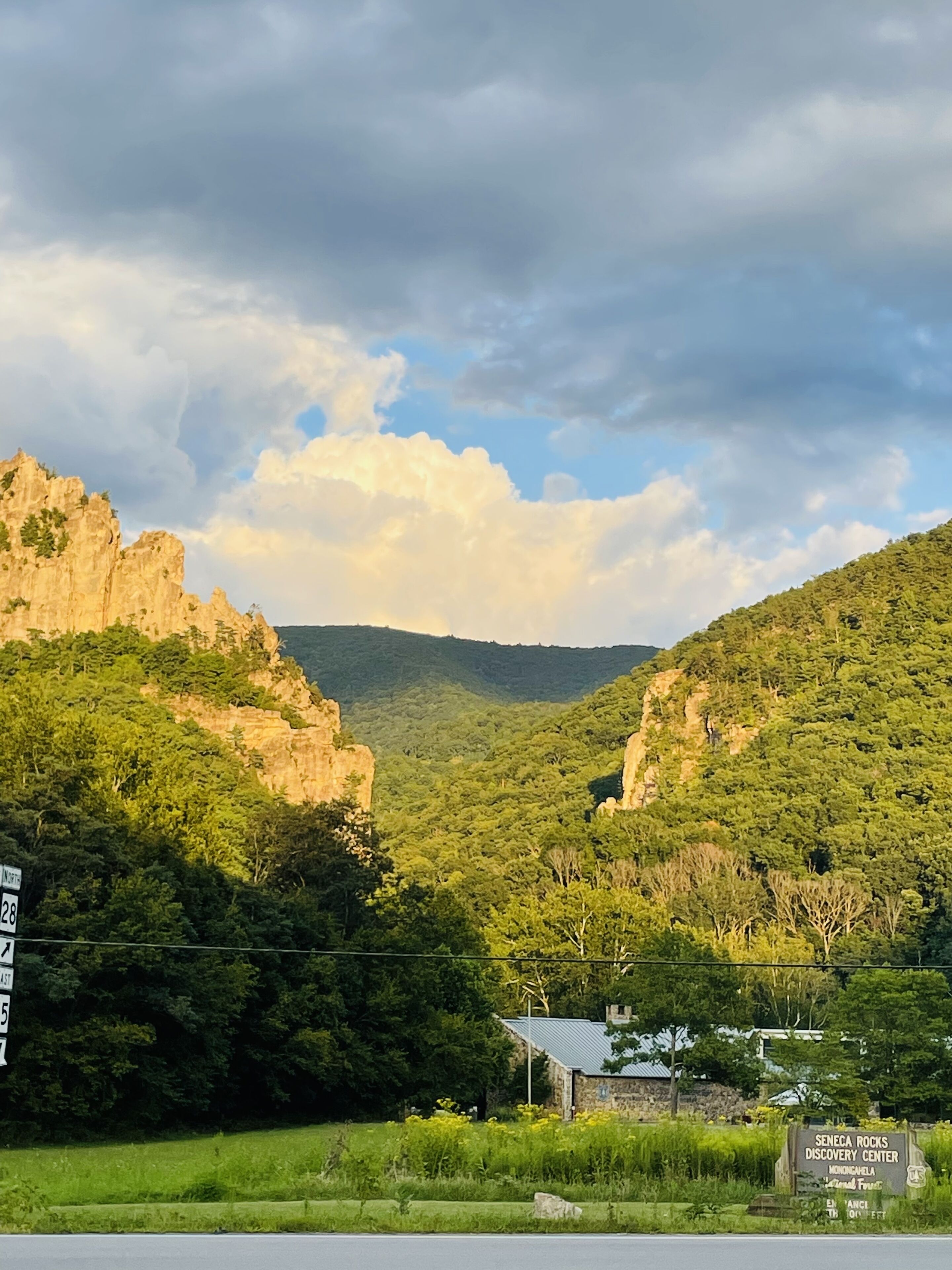Un paysage naturel caractérisé par une falaise rocheuse, une végétation luxuriante et un petit bâtiment portant l’inscription « Centre de découverte de Seneca Rocks ».