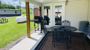 A covered patio with a grill, outdoor seating, and a view of a grassy field.