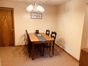 Ein Esszimmer mit Holztisch, vier Stühlen, einer karierten Tischläufer, einem Kerzenhalter und einem Schild an der Wand.