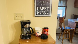 A kitchen area with a coffee maker, coffee pods, a mug rack, and a sign that reads "THIS is my HAPPY PLACE."