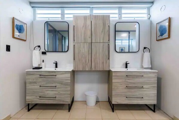 Un baño moderno con dos lavabos, un espejo sobre cada uno y un mueble central.